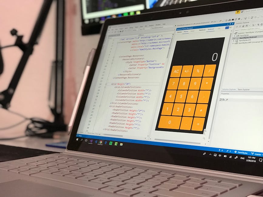A close-up view of a laptop on a desk showing a coding editor with lines of HTML and CSS code on the left side of the screen, and a large, orange numerical calculator interface on the right side with